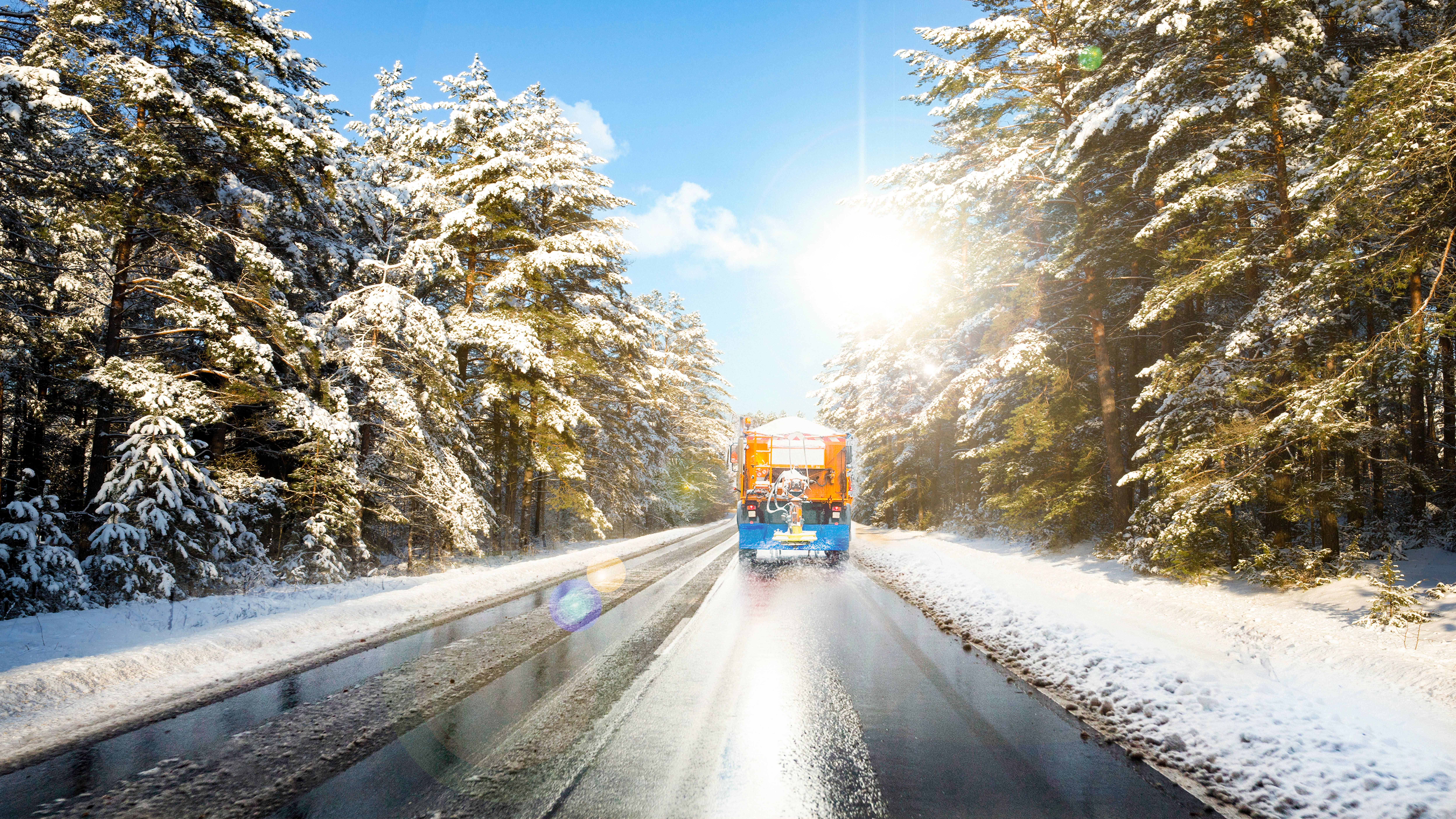 Winter service vehicle travelling along a snow-covered road through a winter forest.