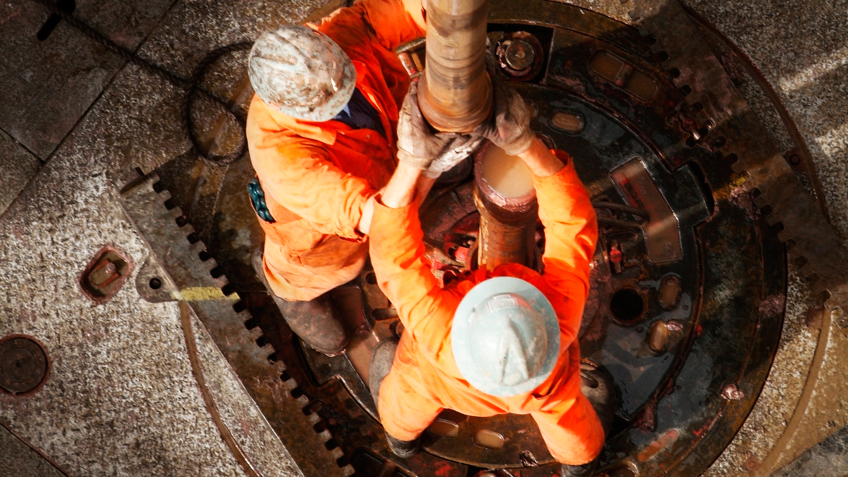 Overhead view of two workers in orange protective clothing securing a pipe on industrial equipment.